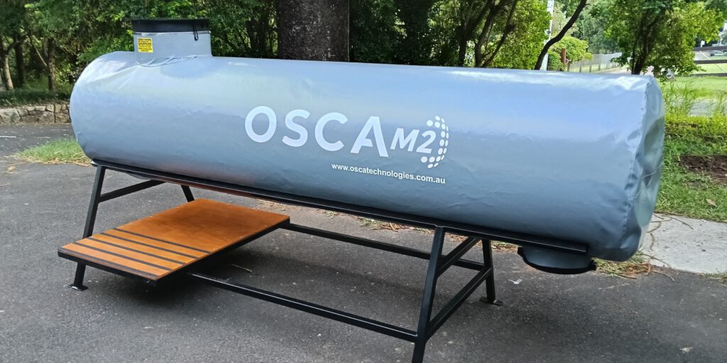 Covered OSCA M2 composter tank with protective weather cover and wooden bench platform, installed outdoors for sustainable organic waste processing and industrial composting operations