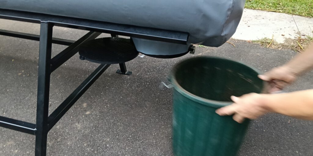 Person holding green collection bin beneath discharge drain of OSCA composter on metal frame, collecting processed compost for sustainable organic waste management and circular economy operations