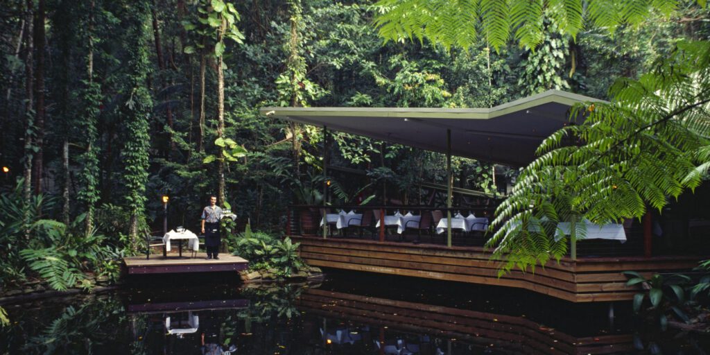 Modern open-air restaurant on wooden decking overlooking pond and tropical forest, showcasing eco-resort hospitality with OSCA composter for sustainable organic waste management and circular economy operations