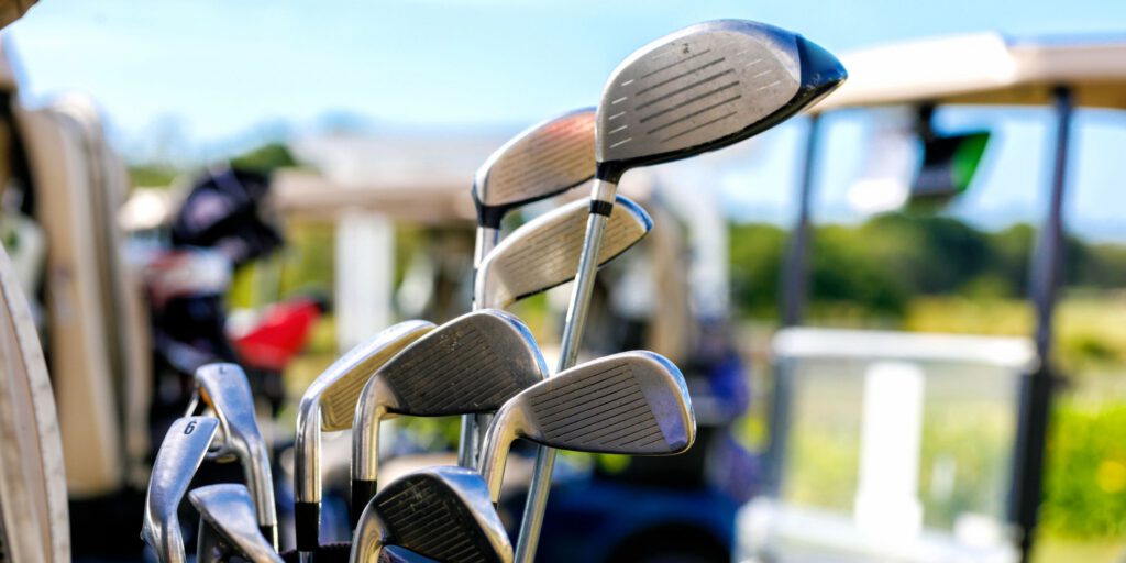 Golf clubs in golf bag with golf buggies and greenery in background, representing the sports and recreation sector where OSCA composter systems provide sustainable organic waste management solutions for golf courses