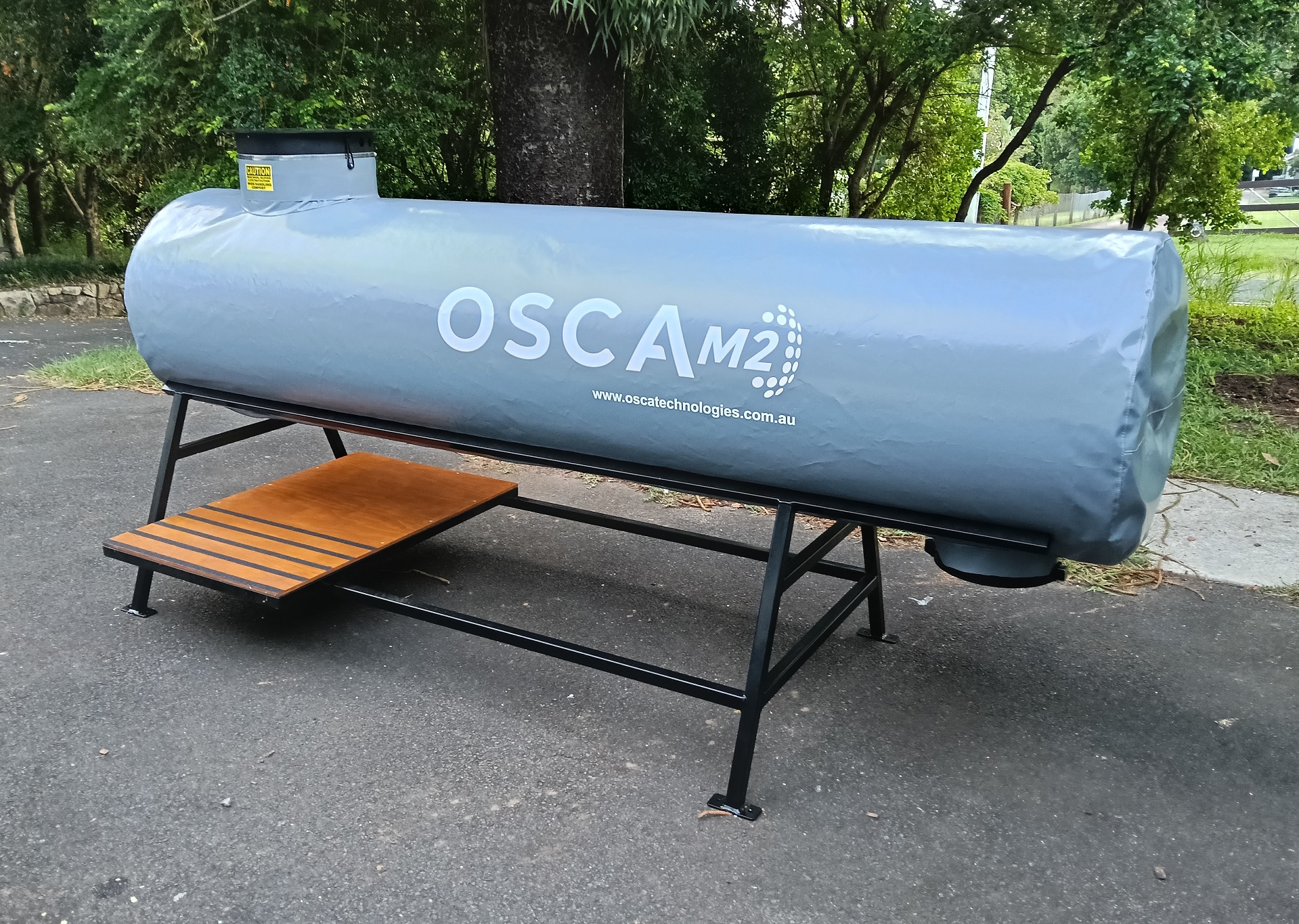 OSCA M2 composter tank mounted on metal frame with wooden platform, outdoor installation for sustainable organic waste processing and composting operations